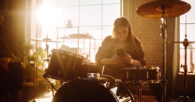 Young Female Pulls out Her Smartphone to Answer a Social Media Message. Expressive Drummer Finished Playing Drums in a Loft Music Rehearsal Studio