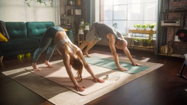 Athletic Young Couple Exercising Together, Stretching and Doing Yoga in the Morning in Bright Sunny Room at Home. Attractive Man and Woman in Sports