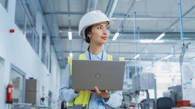 A Happy and Smiling Asian Female Engineer in White Hard Hat Standing with Laptop Computer at Electronic Manufacturing Factory. Successful Employee