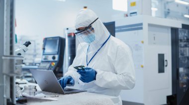 Modern Technology Concept: Engineer in Coverall Working on Laptop Computer, Examining a Circuit Board with Microchips. Electronic Manufacturing