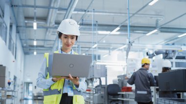 A Happy and Smiling Asian Female Engineer in White Hard Hat Standing with Laptop Computer at Electronic Manufacturing Factory. Successful Employee