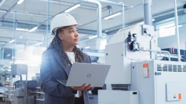 Portrait of an African Female Engineer in Hard Hat Standing and Using Laptop Computer at Electronic Manufacturing Factory. Technician Working on