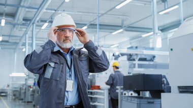 Close Up Portrait of a Middle Aged, Successful Male Engineer in White Hard Hat and Safety Glasses, Standing at Electronics Manufacturing Factory