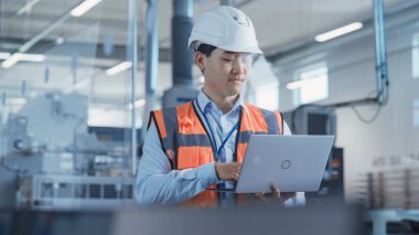 Portrait of an Asian Male Engineer in Orange Safety Vest Working on Laptop Computer at Electronic Manufacturing Factory. Technician Working on Daily