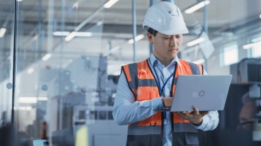 Research and Development Specialist Using Laptop to Operate a Heavy Industry Machine at a Factory. Asian Male Technician Configuring Industrial