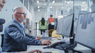 Portrait of a Middle Aged Industrial Engineer Developing Models of a Heavy Industry Machine Parts on Computer CAD Software in a Factory. Modern