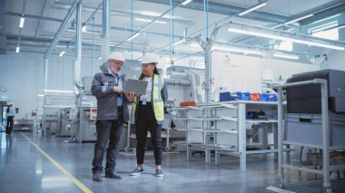 Portrait of Two Heavy Industry Employees in Hard Hats at Factory. Checking and Discussing Industrial Facility, Using Laptop Computer. African American