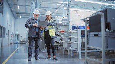 Portrait of Two Heavy Industry Employees in Hard Hats at Factory. Checking and Discussing Industrial Facility, Using Laptop Computer. African American
