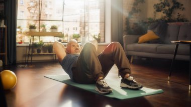 Senior Man Exercising and Training at Home on Sunny Morning. Middle Aged Male Doing Crunches, Stretching Back, Body and Muscles in Loft Stylish