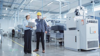 Two Heavy Industry Employees in Safety Uniform and Hard Hats Walking and Talking in a Factory. Asian Engineer and Technician are Discussing Industrial