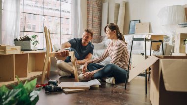 Family Moving in and Home Renovations: Happy Couple Assembles Furniture Together, Girlfriend Reads Instructions and Boyfriend Follows them with some