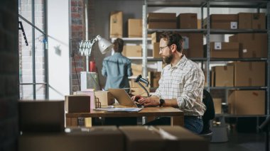 Two Employees Preparing Working on Orders Made from Online Store Sales. Man and Female Working in a Storeroom. Man Using Laptop Computer, Black Woman
