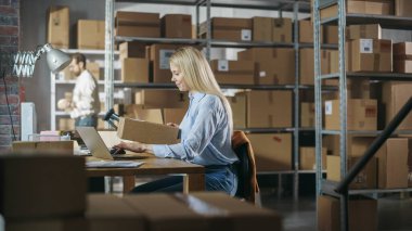 Small Business Owner Comes Over to a Desk with Laptop Computer in Order to Check a Parcel Before Sending It Away to a Client. Working in Logistics