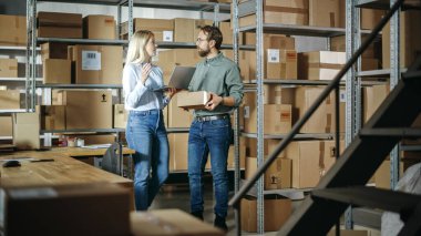 Warehouse Inventory Manager and Worker Walking and Using Laptop Computer, Talking About Parcel Shipment. Small Business Owners Working in Storeroom