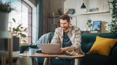 Portrait of Smiling Middle Aged Man Working from Home on a Laptop Computer in Sunny Cozy Apartment. Successful Male Entrepreneur Does Remote for e