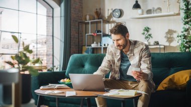 Happy Accounting at Home: Cheerful Smiling Man Using Laptop Computer, Filling Tax Forms. Businessman Solving All His Paperwork Problems: Bills