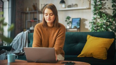 Portrait of Smiling Young Woman Working from Home on Laptop Computer in Sunny Cozy Apartment. Successful Creative Girl Entrepreneur Does Remote for e