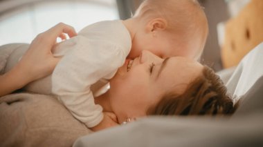 Sevgi Dolu Genç Anne Evde Oynuyor ve Sevimli Bebek Bakımı. Gülümseyen Güzel Anne ve Sevimli Küçük Bebek Yatak Odasında Sarılırken