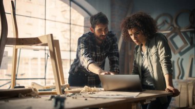 İki Küçük İşletme Sahibi Laptop Bilgisayar Kullanıyor ve Mobilya Atölyesinde Yeni Bir Ahşap Sandalyenin Tasarımı Hakkında Tartışıyor. Marangoz ve Young.