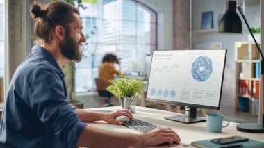 Klas Uzun Sakallı Uzman Yaratıcı Ajans Masasında Oturuyor. Moda Analizi Çizelgeleri ile Masaüstü Bilgisayarı üzerinde Çalışan Genç Tarz Adamı