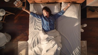 Top View Apartmanı: Güzel Genç Kadın Yatağında Cazibeli Uyuyor, Akıllı Telefon Alarmı Saatini Kapatıyor, Mutluluk ve Gülümsemeyle Yeni Bir Gün Kutluyor