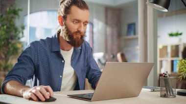 Yaratıcı Ofis Masasında oturan Uzun Saçlı Güzel Sakallı Yöneticinin Portresi. Stil Adam Pazarlama Şirketi 'nde Dizüstü bilgisayar kullanıyor