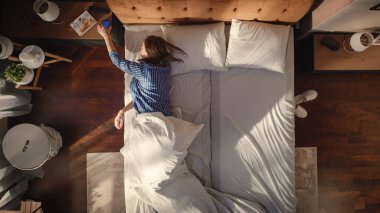 Top View Apartmanı: Güzel Genç Kadın Yatağında Cazibeli Uyuyor, Akıllı Telefon Alarmı Saatini Kapatıyor, Mutluluk ve Gülümsemeyle Yeni Bir Gün Kutluyor