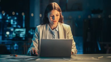 Yetenekli Dijital Pazarlama Uzmanı Akşam Ofisinde Dizüstü bilgisayar üzerinde çalışıyor. Genç İşkadını Yaratıcı Acentede Bilgisayar Kullanıyor, Kontrol Ediyor