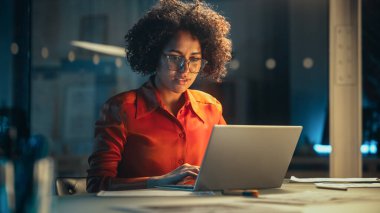 Güzel, çok ırklı Brezilyalı kadın Laptop 'ta gece geç saatlerde çalışıyor. Genç Yaratıcı Müdür ofiste eğleniyor, sohbet ediyor.