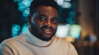 Beyaz balıkçı yakalı yakalı yakışıklı siyah bir adamın yakın portresi, kameraya bakıyor ve mükemmel bir gülümseme sergiliyor. Mutlu Çekici Yönetici