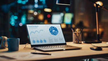 Satış İstatistikleri ve Veri Tablosu Ekranda Gösterilen Masanın Üzerinde duran Dizüstü bilgisayar. Bilgisayarlı masa, kahve fincanı, kulaklık ve defter.