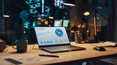 Satış İstatistikleri ve Veri Tablosu Ekranda Gösterilen Masanın Üzerinde duran Dizüstü bilgisayar. Bilgisayarlı masa, kahve fincanı, kulaklık ve defter.