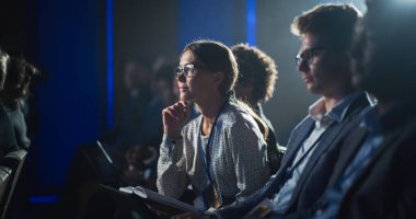 Bir İş Konferansında Kalabalık Seyirci İçinde Oturan Genç Kadın. Dişi katılımcı önemli mermi işaretlerini not defterine yazıyormuş. Keynote