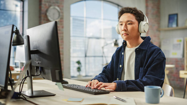 Portrait of Asian Male Employee Working on Computer in a Modern Office During the Day. Customer Support Agent Answering Requests While Using