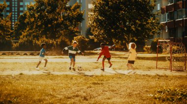 Güneşli bir günde, arka bahçelerinde futbol oynayan çok kültürlü arkadaşlar var. Neşeli oğlanlar ve kızlar dışarıda sporu seviyorlar.