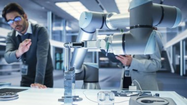 Modern bir Robotik Kol Tutma ve Mekanik Metal Bileşeninin Yakın Çekimi. Çeşitli Mühendis Ekibi Tablet Bilgisayarını kullanarak Yönlendirme