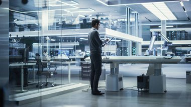 Genç Çoklu Etnik Erkek Mühendis, Yüksek Teknoloji Endüstrisinde Bir Tablet Bilgisayar Kullanıyor, Bir Fütürist Robotik Silah Makinesi Araştırıyor ve Geliştiriyor