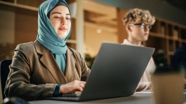Yan yana oturan ve Modern Office 'de dizüstü bilgisayarlar üzerinde çalışan çeşitli yaratıcı genç meslektaşlar grubu. Başarılı bir şekilde Gülümseyen Müslüman Kadın
