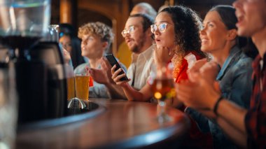 Akıllı Telefon Tutan Heyecanlı Kadın, Bir Bar standında Oturuyor. En sevdiği futbol takımını kurduğu spor bahsi yüzünden gergin. Futbolda Neşeli