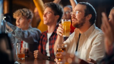 Futbol maçı sırasında spor barında galibiyeti kutlayan mutlu bir gencin portresi. Tezgahta bira yudumlarken, TV 'ye bakarken,