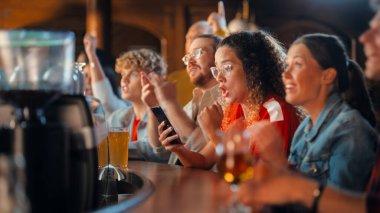 Akıllı Telefon Tutan Heyecanlı Kadın, Bir Bar standında Oturuyor. En sevdiği futbol takımını kurduğu spor bahsi yüzünden gergin. Futbolda Neşeli