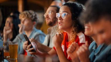 Akıllı Telefon Tutan Heyecanlı Kadın, Bir Bar standında Oturuyor. En sevdiği futbol takımını kurduğu spor bahsi yüzünden gergin. Futbolda Neşeli