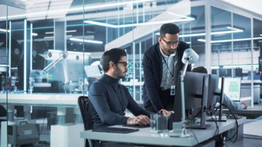 İki Endüstriyel Mühendis Robotik Girişim Tesisinde Çalışma Projelerini Konuşuyor ve Masaüstü Bilgisayarını Kullanıyor. Uzmanlar ve Profesyoneller