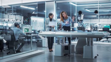 Fabrika Geliştirme Atölyesinde Endüstriyel Programlanabilir Robot Kolu Kullanan İki Kadın Mühendis Profesyonel Çok Kültürlü Ekibi. Robot El