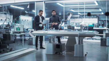 Genç Mühendis, Dizüstü bilgisayarlı Robot Bilimci Meslektaşı 'yla çalışıyor. Bir Endüstriyel Girişim 'de Robot Kolu Geliştirme üzerine işbirliği yapıyorlar.