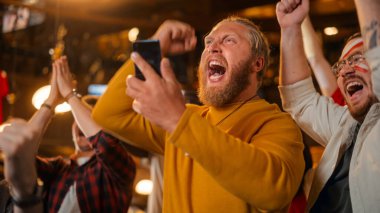 Smartphone 'u tutan kaslı erkek favori futbol takımına koyduğu spor bahsi için gergin. Futbol takımı sayı yaptığında kendinden geçmiş.