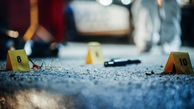 Ters giden gasp olayından sonra suç mahalinde düşük açılı kanıt görüntüsü dağıtıldı. Kanlı gözlük, silah ve kurşunun yanında numaralandırılmış işaretler var.