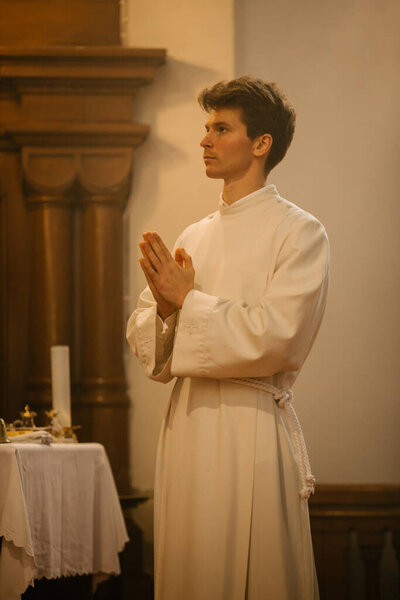Portrait of a Male Young Minister in White Robes Standing Humbly During the Ceremony of Holly Communion. A Servant of God Following the Path of