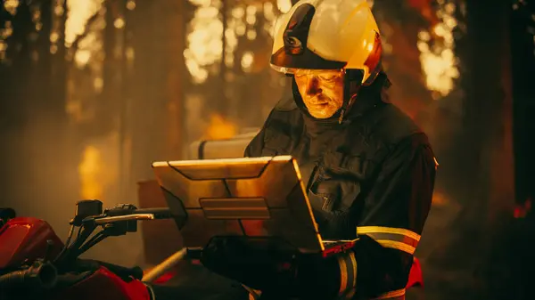 stock image Portrait of a Fireman in Safety Gear Using Heavy-Duty Laptop Computer, Reporting on a Situation with a Dangerous Wildland Fire in a Forest. Hard Day