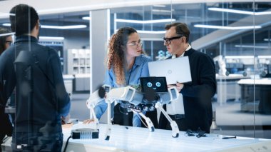 Çeşitli Endüstriyel Robot Uzmanları Mobil bir robotla bir masanın etrafında toplandı. Bilim adamları Tablet ve Laptop Bilgisayarlarını Programlamak İçin Kullanıyor